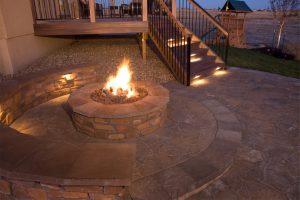 backyard fire pit lit with nearby deck and outdoor lighting