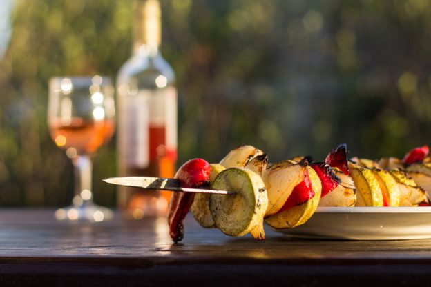 Close up of a table with a veggie kebab and wine glass and bottle.