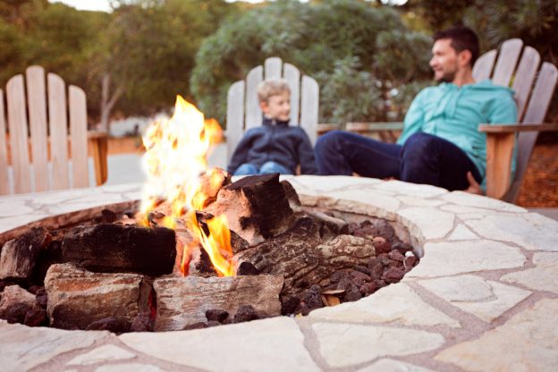 Father and son sitting at a lit, outdoor fireplace.