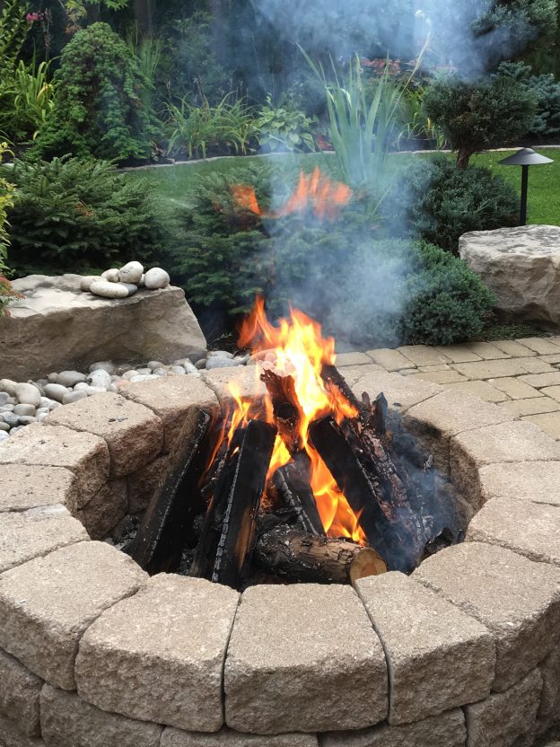 A lit, stone fireplace in a backyard.